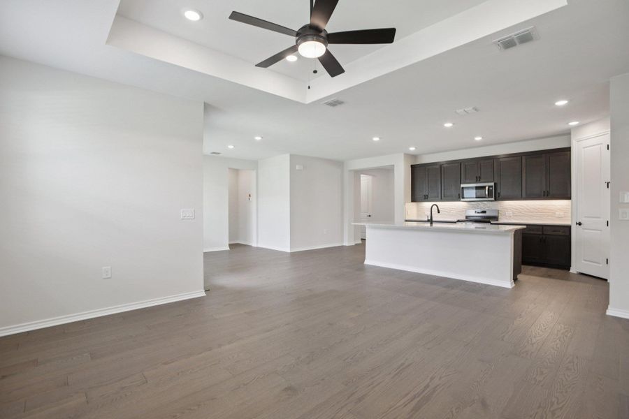 Unfurnished living room with light wood-type flooring, recessed lighting, a tray ceiling, and a ceiling fan