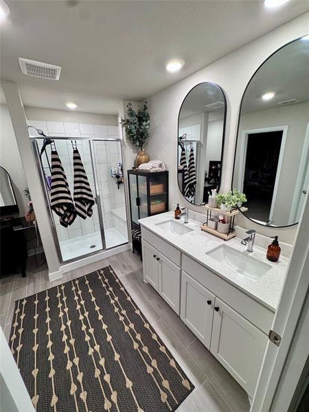 Master bathroom with dual vanity with undermount sinks and quartz-style countertops, separate shower with glass enclosure and white tile surround, wood-finish flooring, recessed lighting, and wall-mounted mirrors