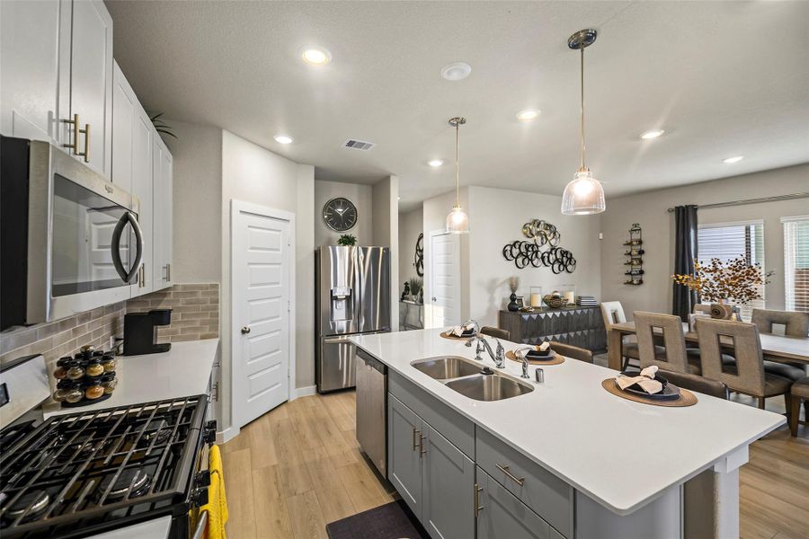 Modern kitchen with sleek stainless steel appliances, a spacious island with dual sinks, and pendant lighting. The open layout flows seamlessly into a stylish dining area, perfect for entertaining.