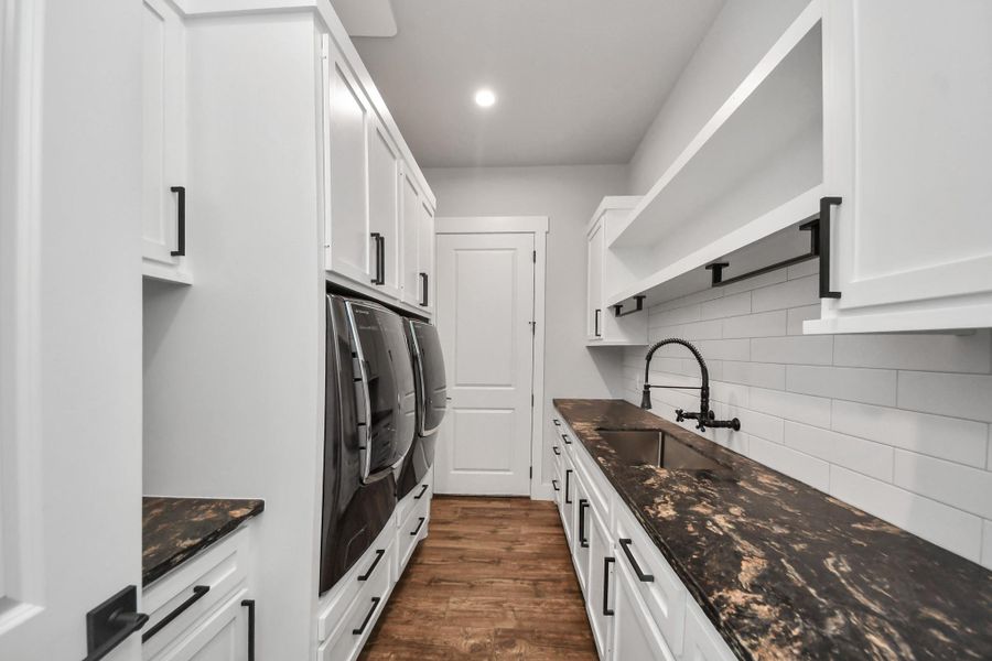 Sleek laundry room featuring modern appliances, elegant black countertops, and abundant white cabinetry for ample storage.