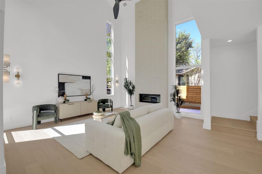 Living area with 24' high ceiling, light wood-style flooring, a large fireplace, and a ceiling fan