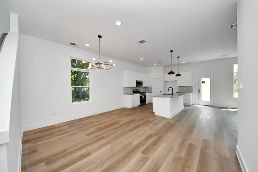 Open-Concept Living & Kitchen – Bright, spacious main living area featuring wood-look flooring, modern lighting, white cabinetry, granite countertops, and a functional kitchen island.