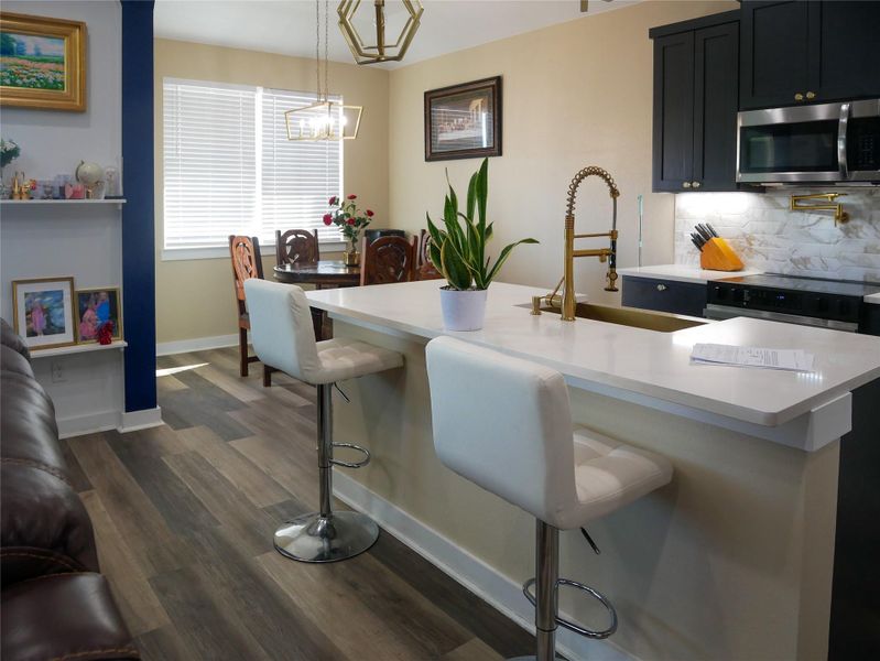 Kitchen featuring a kitchen bar, stainless steel microwave, tasteful backsplash, a kitchen island with sink, and range with electric stovetop
