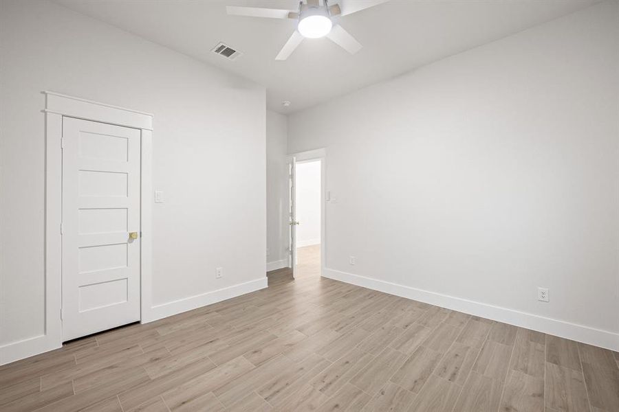 Spacious room featuring light wood-finish flooring, a contemporary ceiling fan with integrated lighting, and a five-panel interior door with brushed gold hardware Spacious room featuring light wood-finish flooring, a contemporary ceiling fan with integrated lighting, and a five-panel interior door with brushed gold hardware