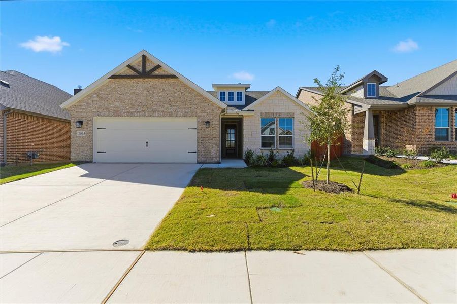 View of front of property featuring a front lawn, driveway, brick siding, and a garage