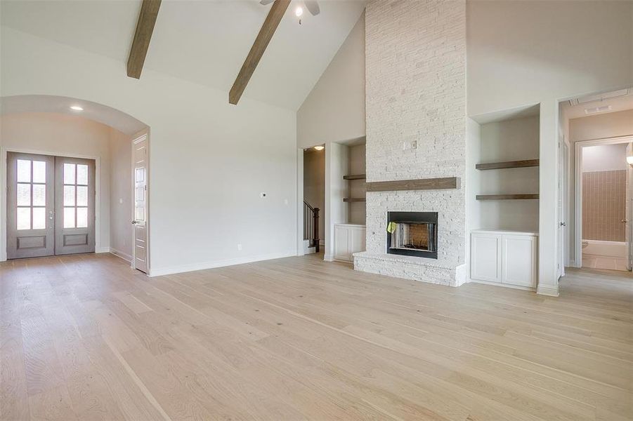 Unfurnished living room featuring beam ceiling, high vaulted ceiling, and light hardwood / wood-style flooring