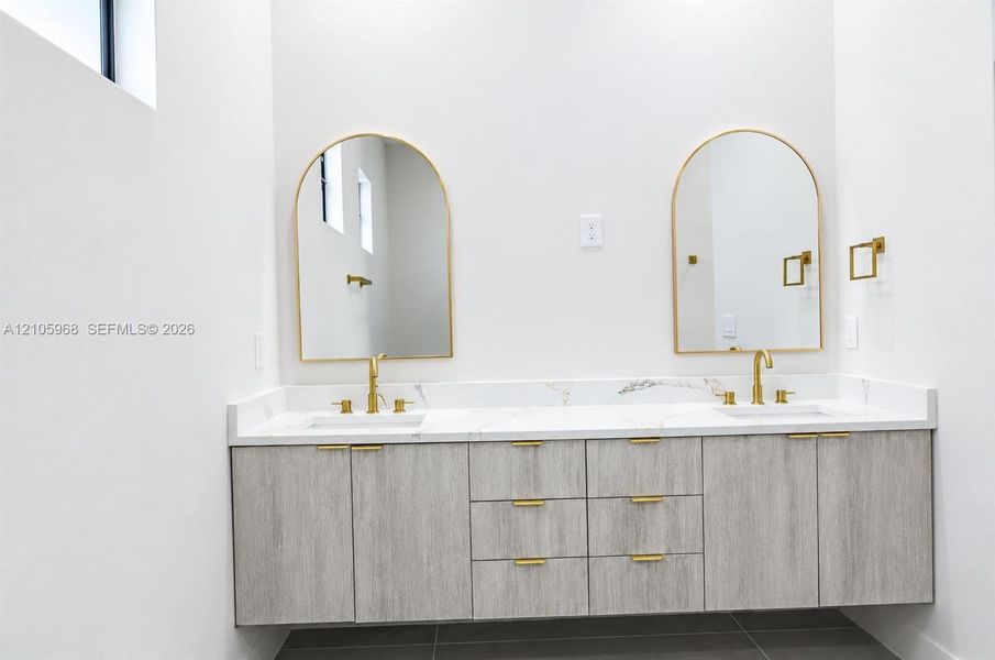 Floating vanity with wood-finish cabinetry, dual undermount sinks, stone-surface countertop, arched mirrors, and brass-tone fixtures