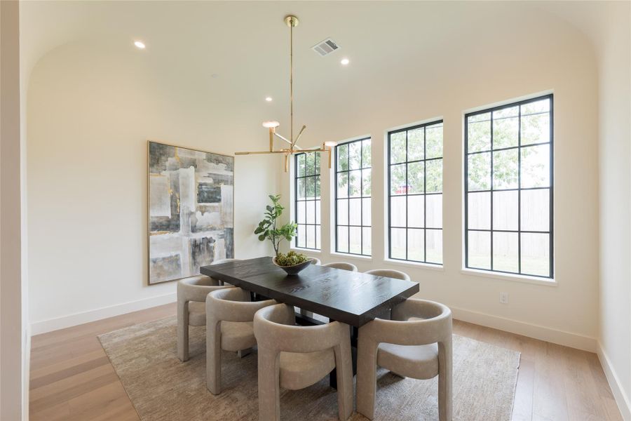 The dining room is defined by its elegant barrel-vaulted ceiling and a trio of oversized dark framed windows that flood the space with natural light. Soft curves, warm European white oak flooring, and an alabaster chandelier create a refined setting that balances architectural symmetry with modern ease. The dining room is defined by its elegant barrel-vaulted ceiling and a trio of oversized dark framed windows that flood the space with natural light. Soft curves, warm European white oak flooring, and an alabaster chandelier create a refined setting that balances architectural symmetry with modern ease.
