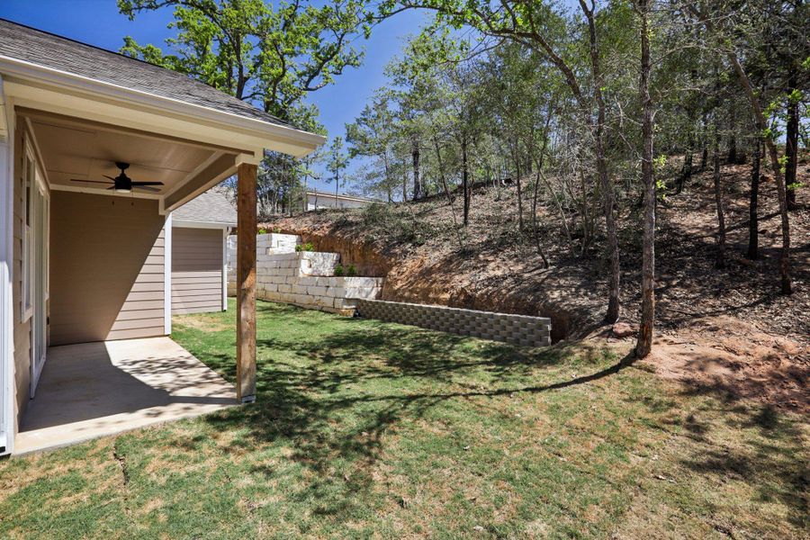 View of grassy yard featuring a patio area, ceiling fan, and  terraced retention wall