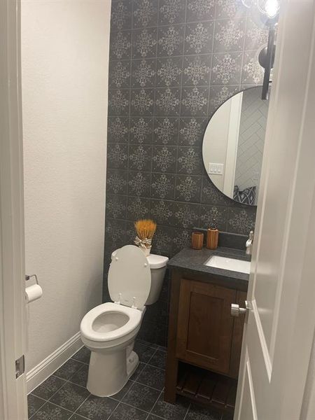 Half bathroom featuring vanity, tile patterned flooring, toilet, baseboards, and decorative backsplash Half bathroom featuring vanity, tile patterned flooring, toilet, baseboards, and decorative backsplash