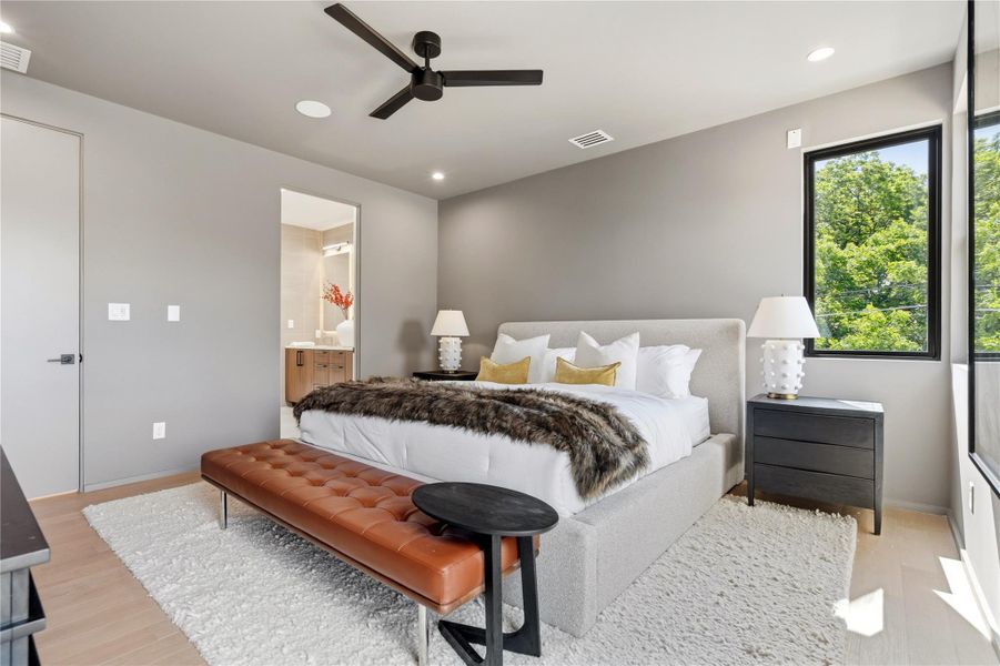 Relax in this well-lit primary bedroom featuring a contemporary ceiling fan and light wood flooring.
