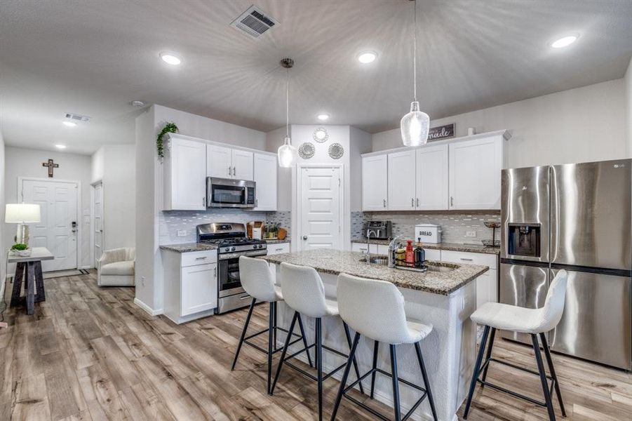 Kitchen featuring stainless steel appliances, a breakfast bar, white cabinets, light stone counters, and a kitchen island with sink