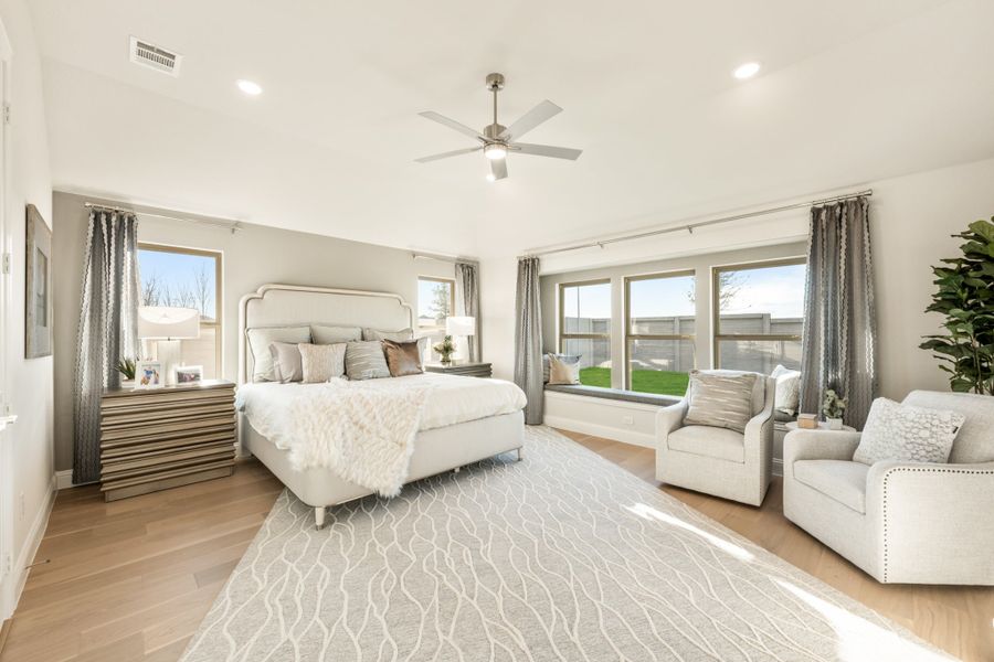 Spacious master bedroom with king bed, ceiling fan, hardwood floors, and window seating area
