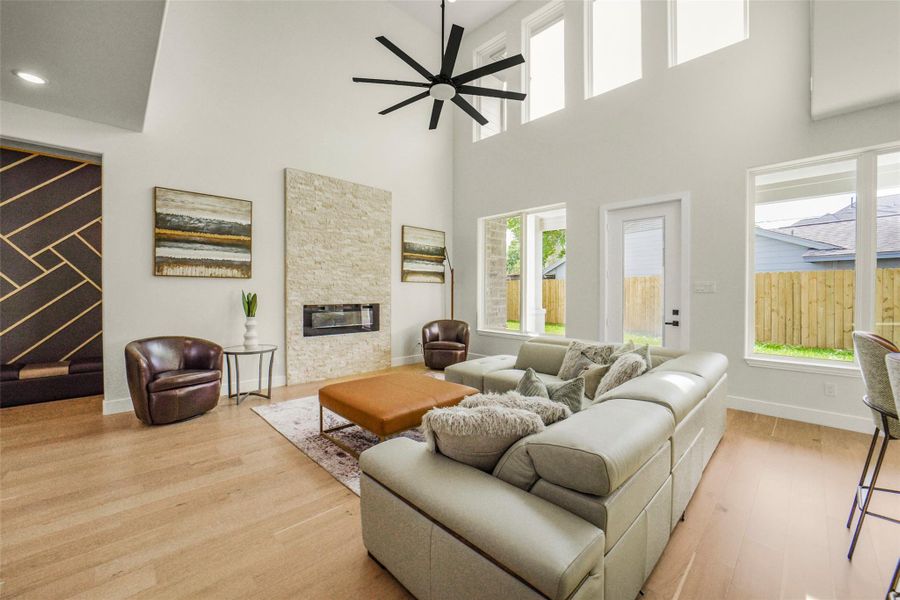 Spacious living room with high ceilings, large windows, and abundant natural light. Features a modern fireplace, light wood flooring, and stylish decor. Cozy seating area ideal for relaxation and entertaining.