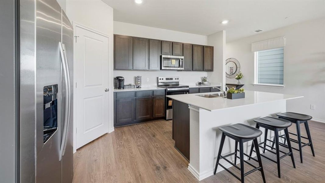 Kitchen with appliances with stainless steel finishes, an island with sink, dark wood-style floors, a breakfast bar, and dark brown cabinetry Kitchen with appliances with stainless steel finishes, an island with sink, dark wood-style floors, a breakfast bar, and dark brown cabinetry