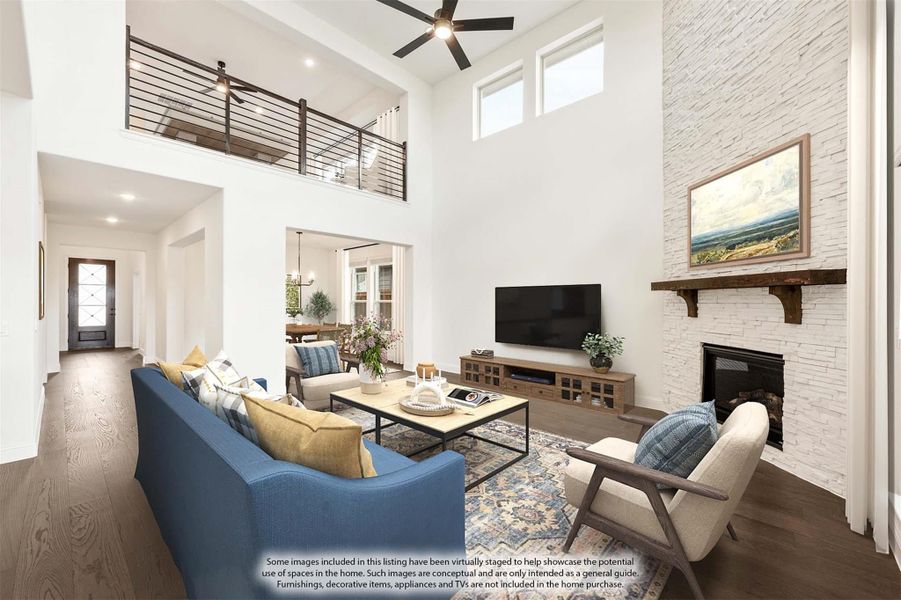 Living room with two-story ceiling, stone fireplace, hardwood floors, and open second-floor loft railing above