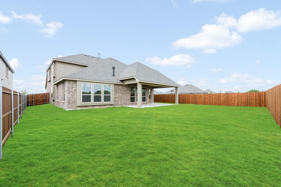 Backyard of brick home with covered patio, large green lawn, and wood privacy fence Backyard of brick home with covered patio, large green lawn, and wood privacy fence