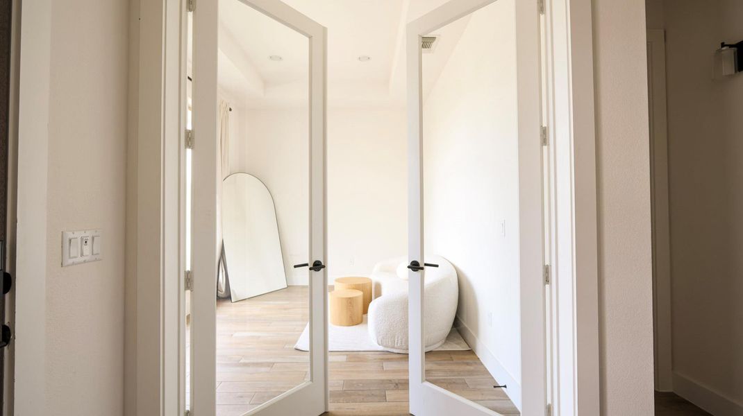 French doors open into a bright room with high ceilings and light wood flooring. French doors open into a bright room with high ceilings and light wood flooring.
