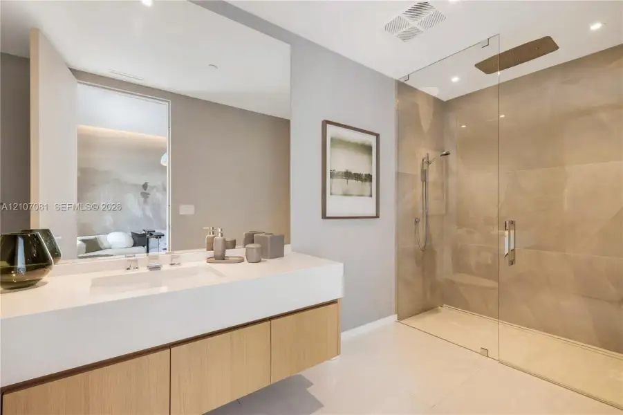 Floating vanity with integrated sink and stone-composite countertop, large-format tiled walk-in shower with frameless glass enclosure, ceiling-mounted rainfall showerhead, and expansive wall-to-wall mirror Floating vanity with integrated sink and stone-composite countertop, large-format tiled walk-in shower with frameless glass enclosure, ceiling-mounted rainfall showerhead, and expansive wall-to-wall mirror