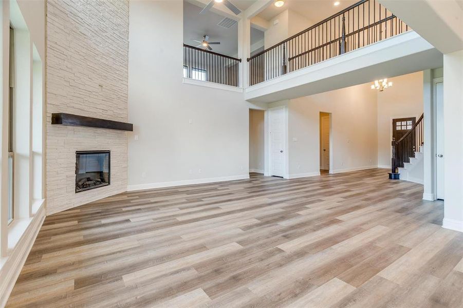 Unfurnished living room with a fireplace, a towering ceiling, ceiling fan with notable chandelier, and light hardwood / wood-style floors