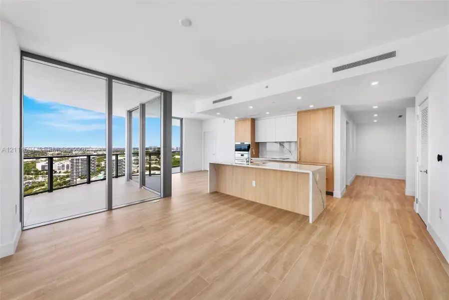 Open-concept interior featuring wood-finish flooring, floor-to-ceiling glass panel walls, a wraparound balcony, a kitchen island with stone-finish countertops, and minimalist flat-panel cabinetry Open-concept interior featuring wood-finish flooring, floor-to-ceiling glass panel walls, a wraparound balcony, a kitchen island with stone-finish countertops, and minimalist flat-panel cabinetry