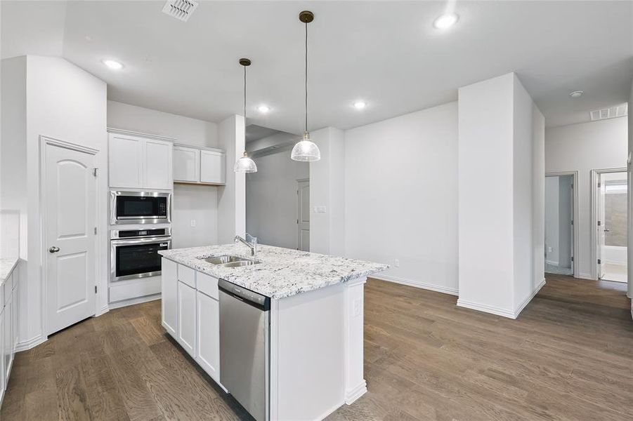 Kitchen with stainless steel appliances, light stone countertops, a center island with sink, white cabinetry, and dark wood-type flooring