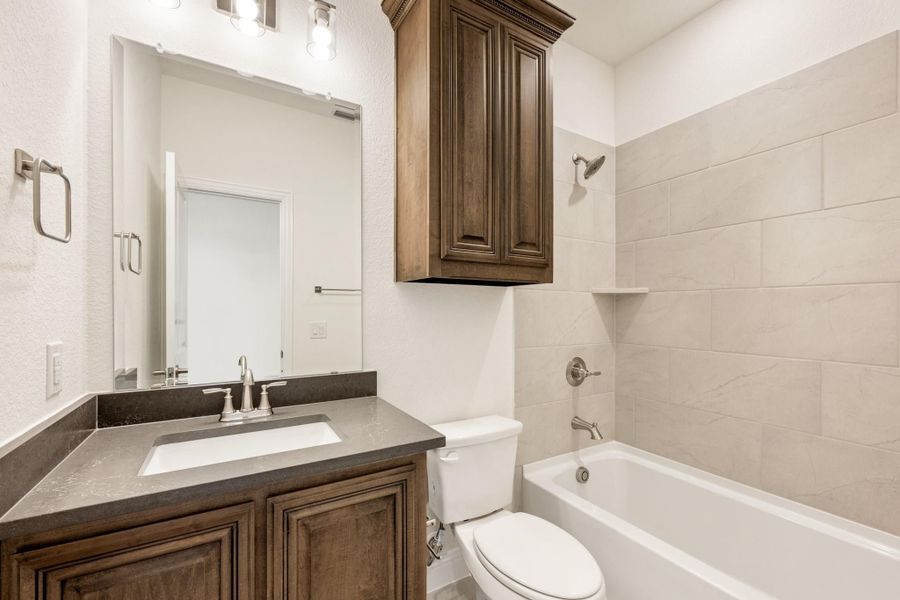 Bathroom with dark wood vanity, dark countertop, and tiled shower-tub combo with wall cabinet above toilet Bathroom with dark wood vanity, dark countertop, and tiled shower-tub combo with wall cabinet above toilet