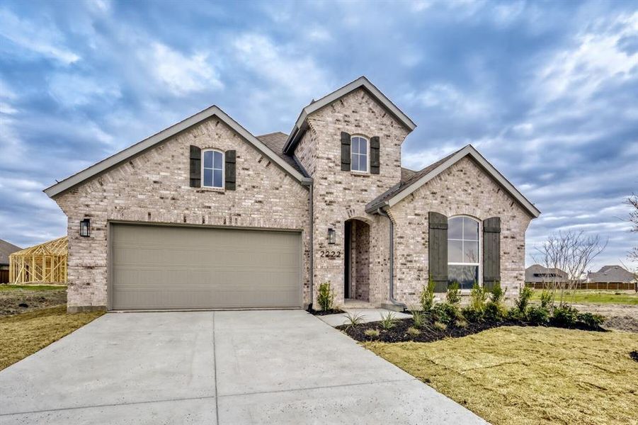 French country inspired facade featuring driveway, brick siding, a front lawn, and an attached garage