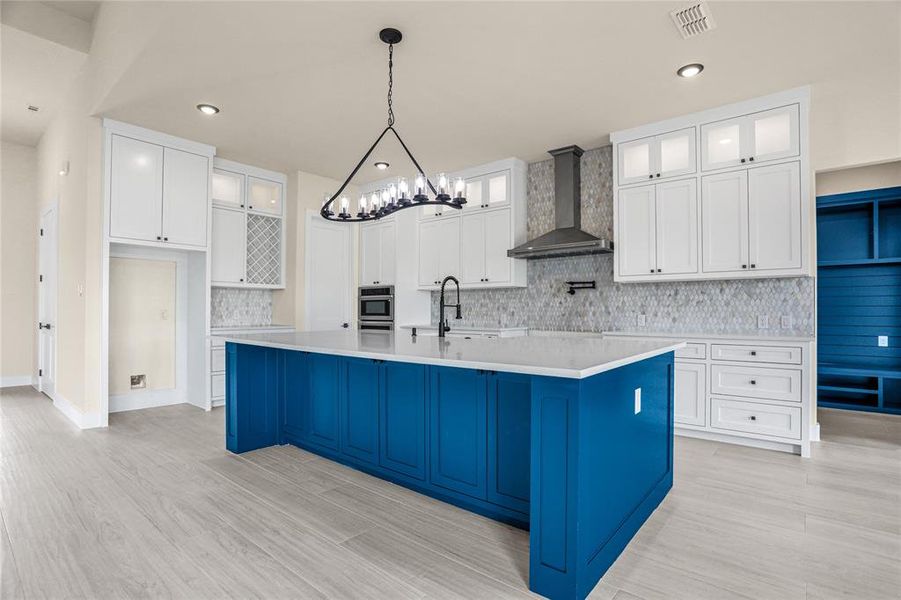 Kitchen featuring wall chimney range hood, decorative backsplash, stainless steel oven, a spacious island, and a chandelier Kitchen featuring wall chimney range hood, decorative backsplash, stainless steel oven, a spacious island, and a chandelier