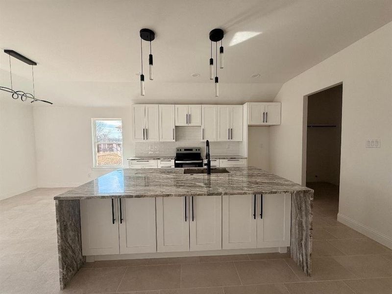 Kitchen featuring white cabinetry, light stone counters, a spacious island, stainless steel range with electric cooktop, and lofted ceiling