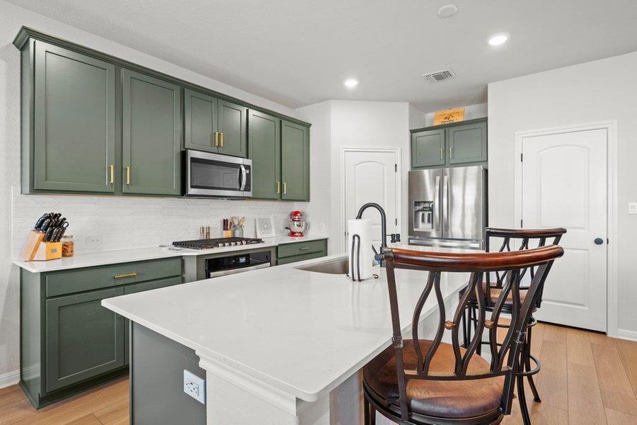 Kitchen with green cabinets, light wood-style flooring, a kitchen bar, an island with sink, and recessed lighting