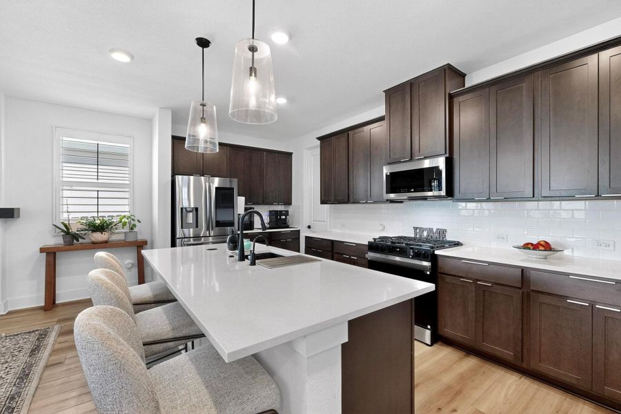 Kitchen featuring espresso cabinets, a kitchen breakfast bar, appliances with stainless steel finishes, decorative light fixtures, and a kitchen island with sink