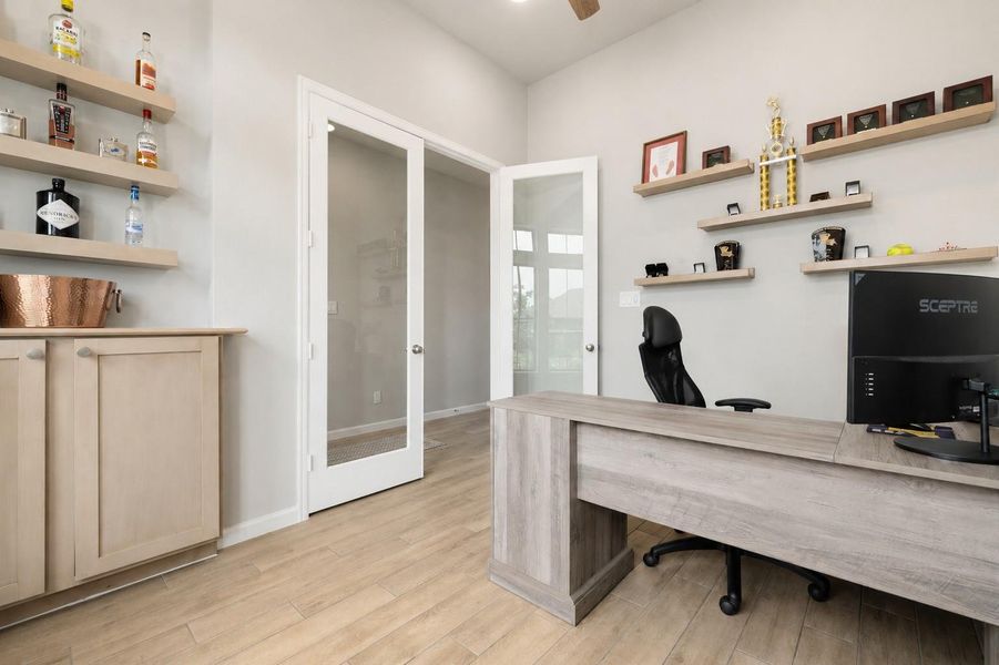 Private home office with glass-paneled doors & large windows for natural light.