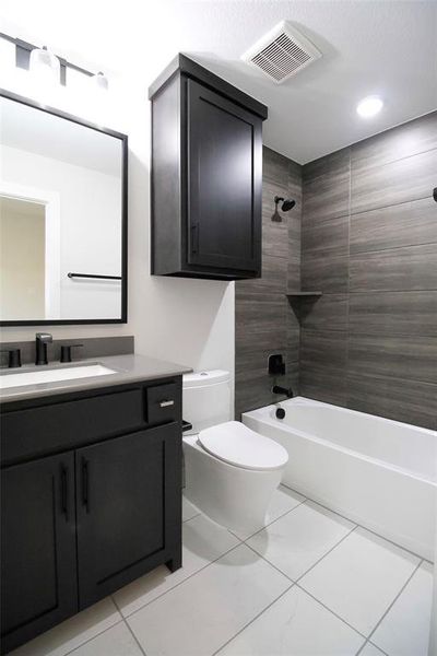 Full bathroom with tile patterned floors, vanity, tiled shower / bath combo, and toilet