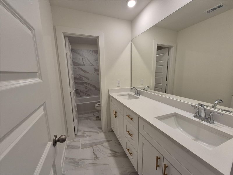 Elegant bathroom featuring a double vanity with sleek white countertops, ample storage, and a stylish tiled bathtub area.