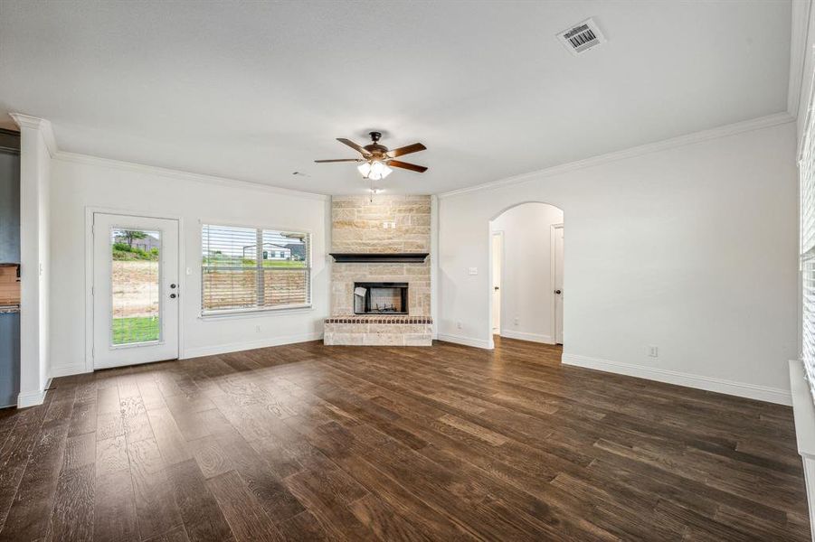 Unfurnished living room featuring ceiling fan, a stone fireplace, crown molding, and dark wood-type flooring