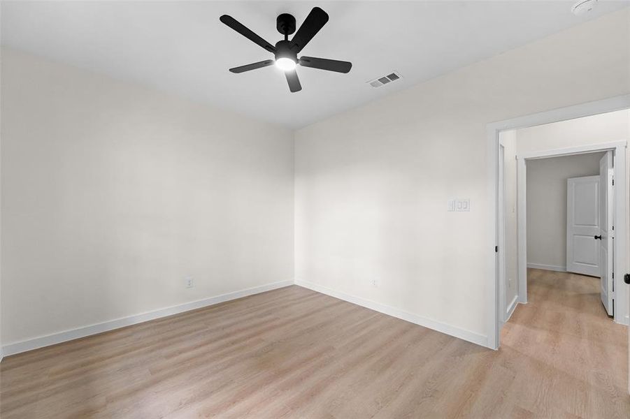 Spacious room featuring wood-finish flooring, white baseboards, and a modern black ceiling fan with integrated lighting Spacious room featuring wood-finish flooring, white baseboards, and a modern black ceiling fan with integrated lighting