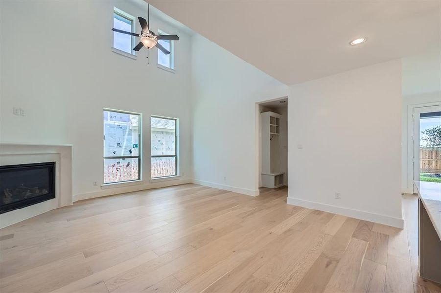 Unfurnished living room with a high ceiling, ceiling fan, and light hardwood / wood-style floors