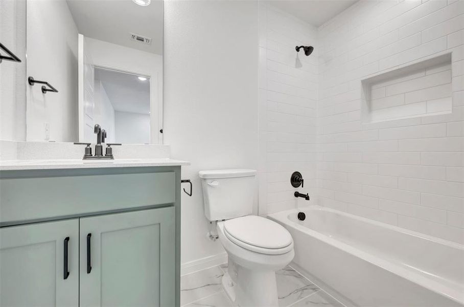 Bathroom featuring a sage green vanity with a white countertop, matte black fixtures, subway tile tub surround with a recessed niche, and marble-look floor tiling