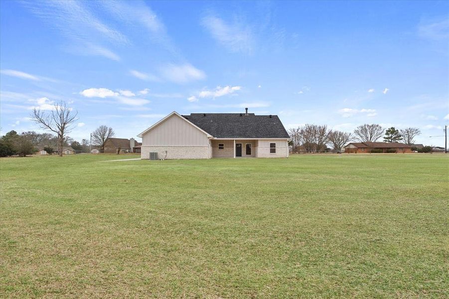 Rear view of house featuring a yard and central AC unit