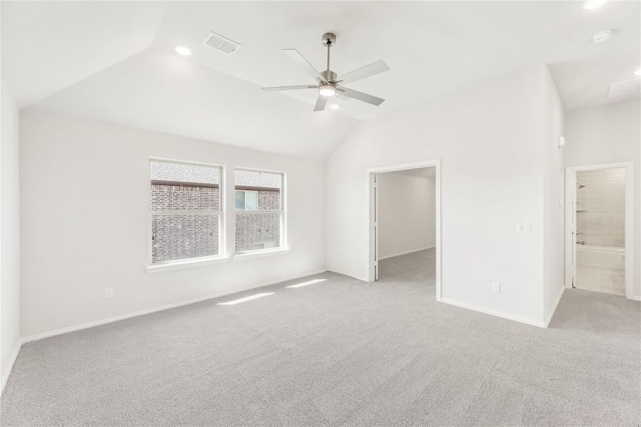 Empty bedroom with vaulted ceiling, ceiling fan, gray carpet, and doors to closet and bathroom Empty bedroom with vaulted ceiling, ceiling fan, gray carpet, and doors to closet and bathroom