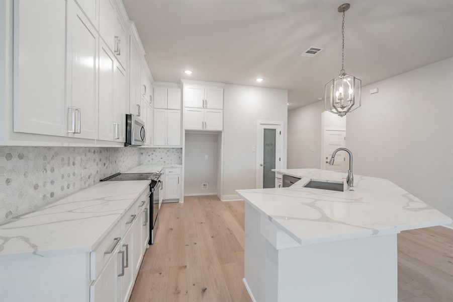 Kitchen with electric stove, a center island with sink, light wood-style floors, light stone counters, and white cabinetry