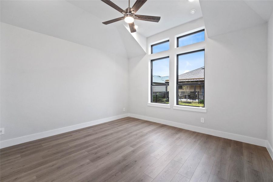 Relax and unwind after a long day in this impressive primary suite! This generously sized room offers laminate flooring, neutral-toned paint, high sloped ceilings with a ceiling fan, and large windows for added comfort and tranquility.