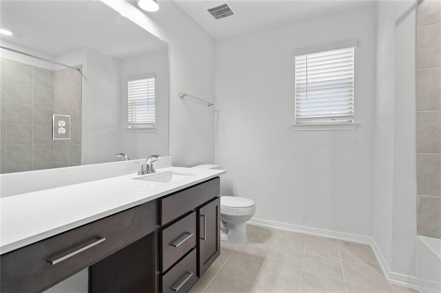 Secondary bath features tile flooring, bath/shower combo with tile surround, stained wood cabinets, beautiful light countertops, mirror, sleek fixtures and modern finishes.