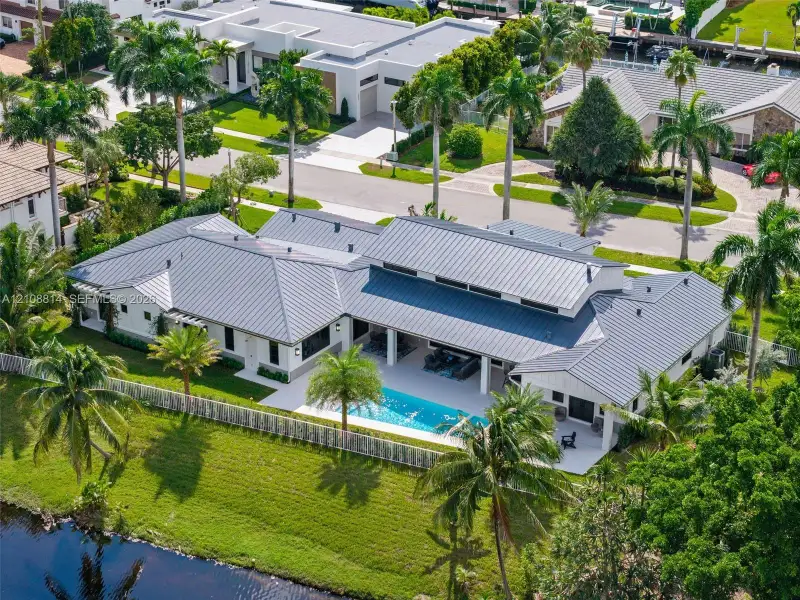 Single-story residence featuring a metal roof, rear swimming pool, covered patio, white exterior finish, and waterfront lot Single-story residence featuring a metal roof, rear swimming pool, covered patio, white exterior finish, and waterfront lot