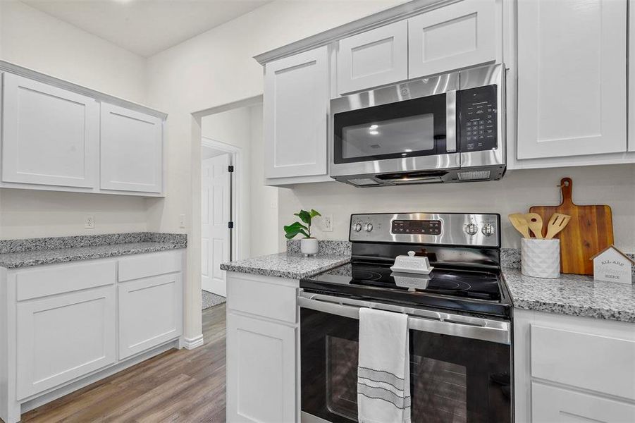 Kitchen featuring white cabinets, appliances with stainless steel finishes, light stone countertops, and light hardwood / wood-style flooring