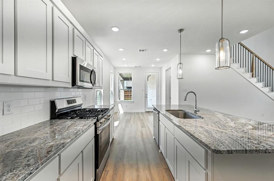 Kitchen featuring dark stone counters, appliances with stainless steel finishes, an island with sink, light wood-style flooring, and backsplash