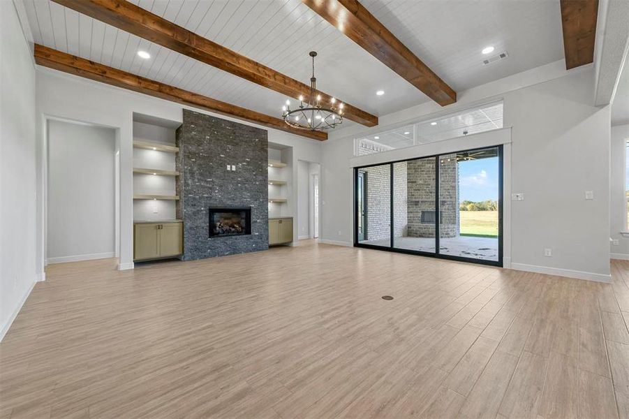 Unfurnished living room with an inviting chandelier, a stone fireplace, light wood-type flooring, beamed ceiling, and wood ceiling