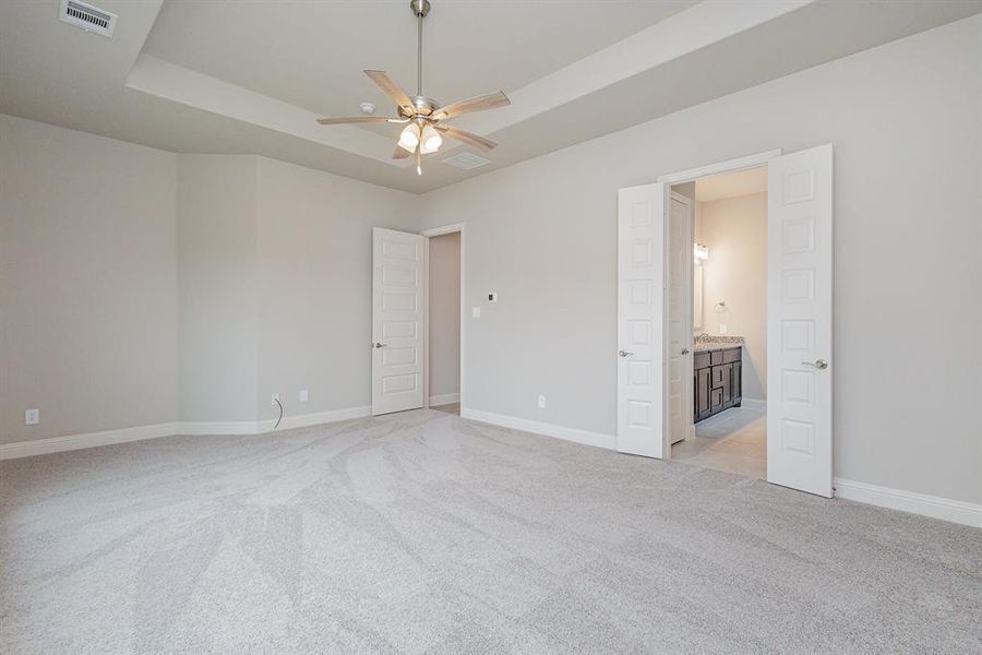 Unfurnished bedroom featuring light colored carpet, a raised ceiling, ceiling fan, and ensuite bathroom