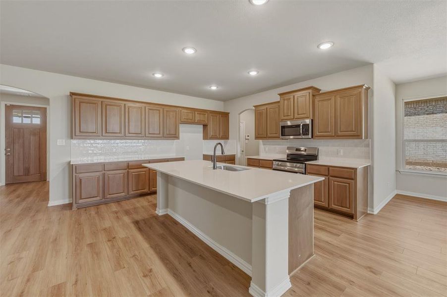 Open-concept kitchen featuring an expansive center island with an integrated sink, wood-finish flooring, and recessed lighting Open-concept kitchen featuring an expansive center island with an integrated sink, wood-finish flooring, and recessed lighting
